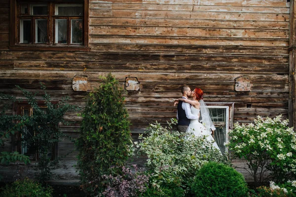 Vášnivý novomanželský pár líbání rty před starou dřevěnou zdí domu — Stock fotografie