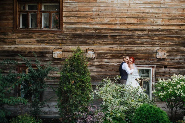 Frisch vermähltes Paar umarmt sich friedlich vor einer alten hölzernen Häuserwand — Stockfoto