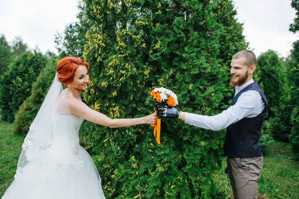 Pareja recién casada intercambiando ramo, posando para una foto en un parque de enebros —  Fotos de Stock