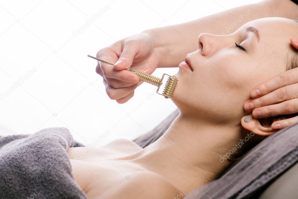 Gliding face roller against chin during gua sha face massage at beauty clinic.