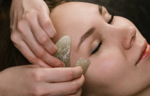 Jovem mulher tendo uma massagem facial gua sha na clínica de beleza asiática. Vista lateral — Fotografia de Stock