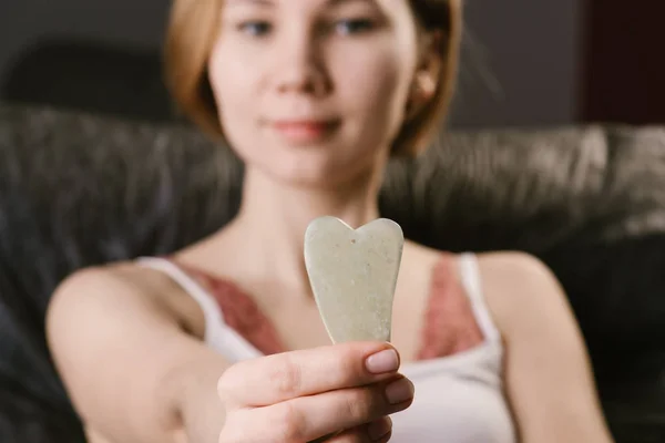 Gua sha massage jade stone presented by a young woman. At home.