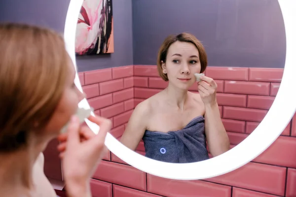 Junge Frau massiert ihr Gesicht mit Gua-sha-Stein in ihrem Badezimmer — Stockfoto