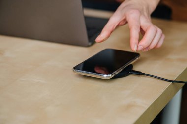 Dizüstü bilgisayarla çalışırken telefonuna uzanan bir kadın el.