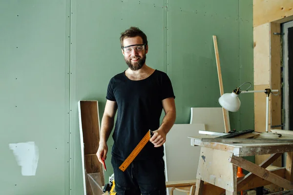 Handsome smiling bearded man standing with corner ruler in rennovating apartment