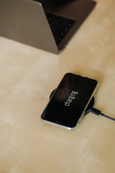 Phone on a charger pad on a table next to laptop