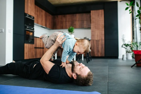 Šťastný otec si hraje se svým dítětem na podlaze a zvedá ho do vzduchu. — Stock fotografie