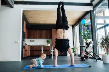 Adam, neşeli bebeğinin yanında el duruşu yapıyor.