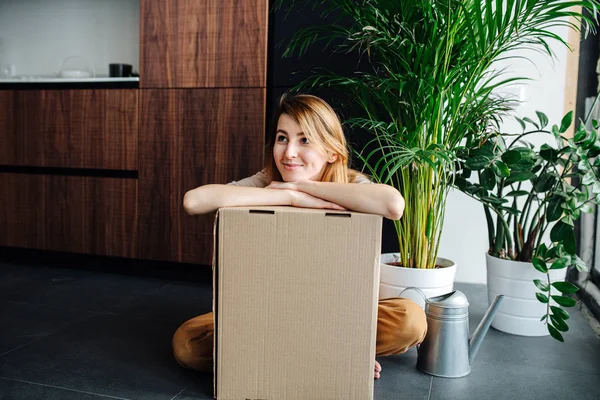 Mujer joven sentada en el suelo, apoyada en una gran caja de cartón en casa — Foto de Stock