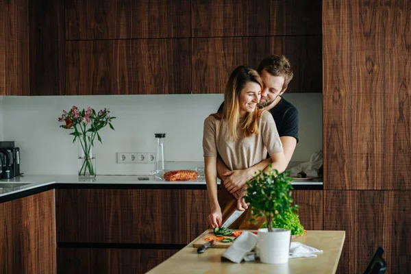 Man seeks attention, hugging his girlfriend while she's slicing vegetables — Stock Photo, Image