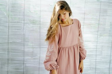 Pembe Midi elbiseli, dağınık saçlı, parlak bir odada duran güzel bir genç kadın. Aşağıya bakıyorum..