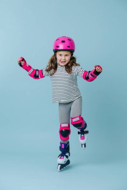 Genç patenci tek ayak üzerinde dururken dengesini koruyor, stüdyoda izole edilmiş mavi bir arka planda.