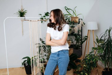 Kız evin içinde poz veriyor, arkasında bir sürü bitki var. Makrome yapmaya hazırlanmıştı..