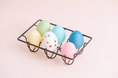 Pembe yüzey üzerinde metal çerçeveli yumurta tutacağı üzerinde altı renkli paskalya yumurtası. Yüksek açı