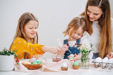 Genç anne, iki kızını evde bir masanın arkasında fırçayla paskalya yumurtası boyarken izliyor. Küçük olan annesine yaslanır..