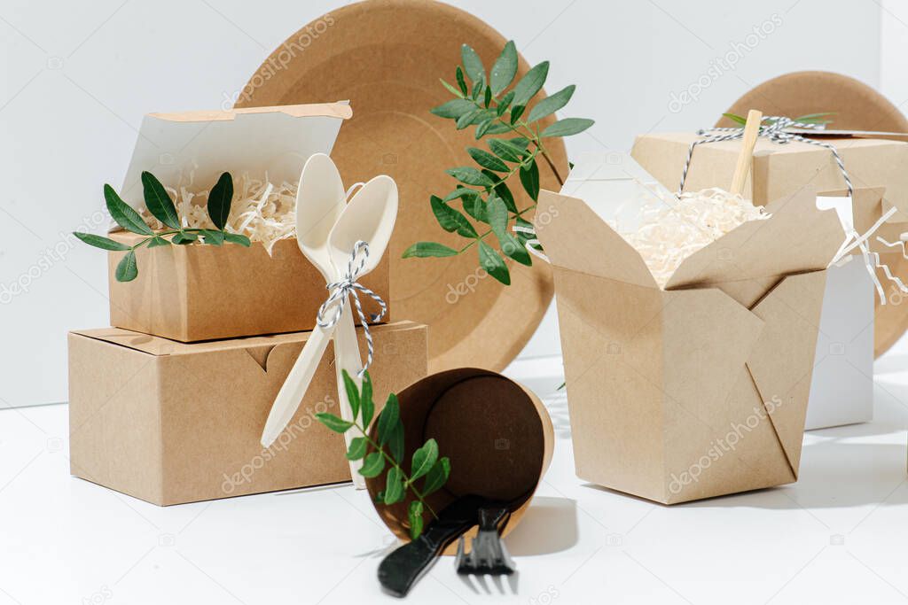 A close-up set of eco-friendly tableware packaging decorated with leafs, and cutlery made of corn starch on a white background