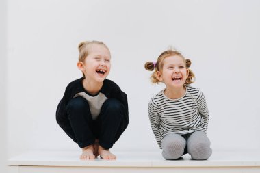 Oyuncu erkek ve kız kardeş, evin beyaz arka planında oturup gülüyorlar.