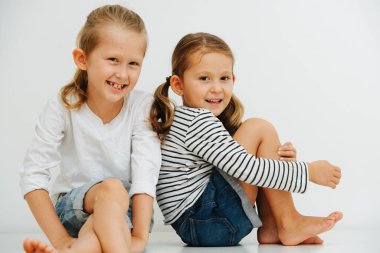 Erkek ve kız kardeşlerin ortak bir portresi, beyaz arka planda günlük giysiler içinde yan yana oturuyorlar.