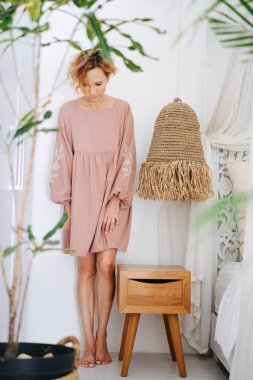 Genç çıplak ayaklı bir kadın komodinin yanında duruyor ve abajur takıyor, yere bakıyor. Üzücü, küçük ve kendinden nefret eden.