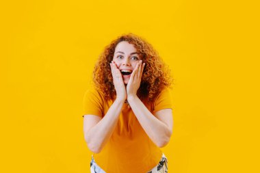 Sarı tişörtlü, kırmızı saçlı kıvırcık kızın olumlu duyguları, sarı arka planda yakın plan portresi.