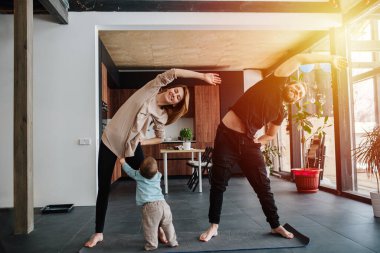 Aile yoga yapıyor, karantina için evde kalıyor. Anne ve baba sabah egzersizlerinin bir parçası olarak yan yatarken, çocukları da annesinin gömleğini çekiştirip ilgi istiyor..