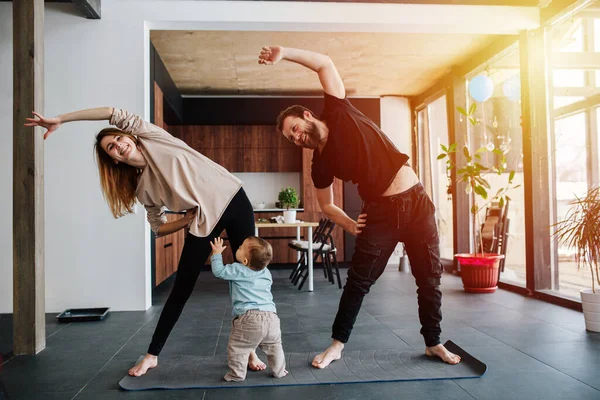 Aile yoga yapıyor, aile hayatı tecrit altında. Anne ve baba egzersiz yapıyor ve bebek çocuk da ailesinin yanında sürünüyor. Pencerelerden gün batımı ışığı