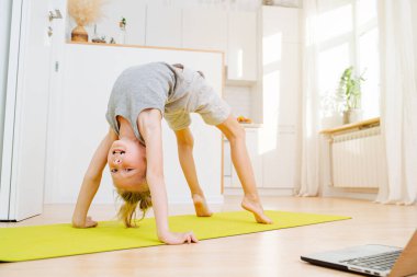 Tatlı küçük çocuk köprü egzersizi yapıyor, kameraya bakıyor. Evde izolasyon üzerine fiziksel atletik egzersiz.