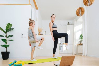 Anne ve oğlu evde dizüstü bilgisayarın önünde yoga yapıyorlar, tek ayak üstünde duruyorlar. Evde kalırken formda kalmak. Ekrana yakından bakıyorum..