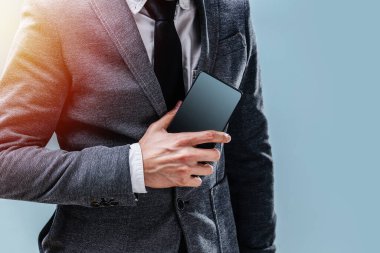 Takım elbiseli genç bir adam elinde bir telefon tutuyor. Mavi arkaplandaki boş ekran yakın plan