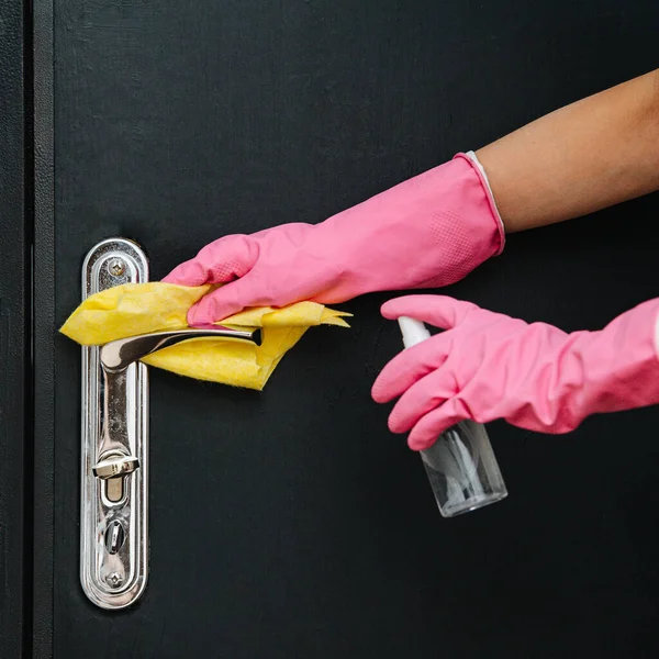 Hands in gloves cleaning standart entrance door handle with a lock. Spraying agent and wiping it. One of things you need to keep clean during covid-19 pandemic.