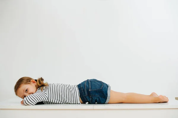 Feliz Sorrindo Menina Descalça Deitada Uma Mesa Sobre Parede Branca — Fotografia de Stock