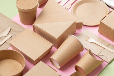 Pembe ve yeşil arka planda çevre dostu tek kullanımlık bulaşık takımı ve bambu kaplar. Kağıt ve mısır nişastası kutuları, fincanlar, paketler ve tabaklar.