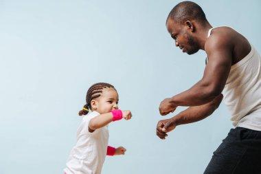 Babası küçük kızını boks için eğitiyor, ciddi bir yüz ifadesi takınıyor. Covid-19 kapanırken kendilerini eğlendiriyorlardı. Mavi üzerine