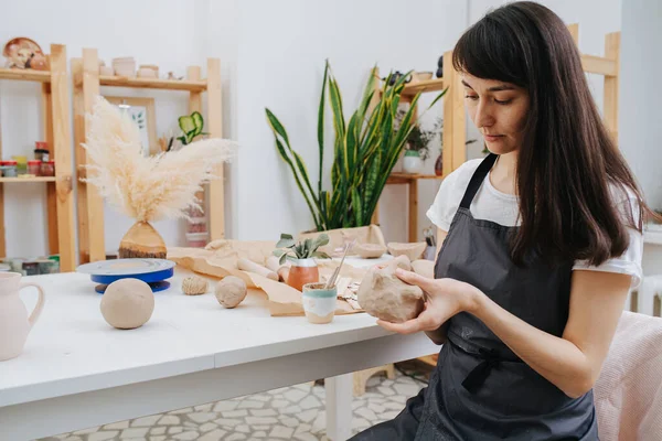 Brunette woman molding clay into shape in her private workshop. Chance to spent time on her hobby during isolation.