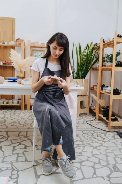 Brunette woman molding clay into shape in her private workshop. Chance to spent time on her hobby during isolation.