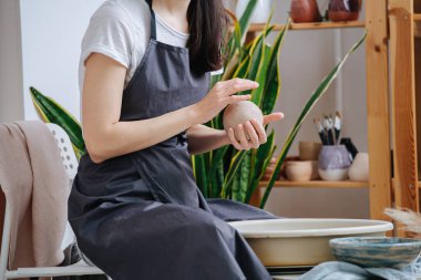 Esmer kadın, gelecekteki atölyesinde vazo yapmak için çömlek çarkının yanında kil şekillendiriyor. İzolasyon sırasında hobisi üzerinde zaman geçirme şansı..