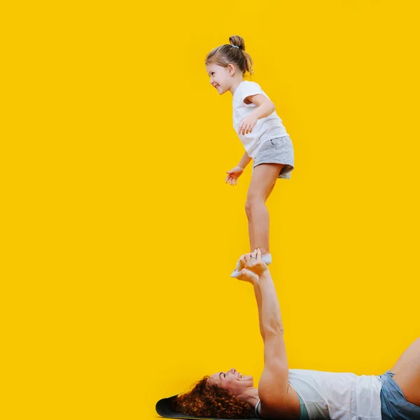 母亲和女儿在黄色背景的瑜伽垫上形成了华丽的造型 女孩高高地站在妈妈的手上 — 图库照片