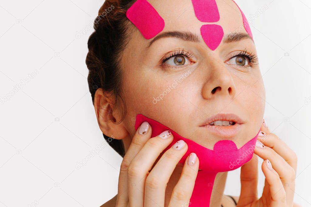 Young woman with pink anti-wrinkle cosmetic tape on her face over white. Double chin reducing.