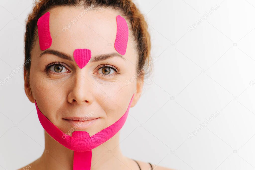 Young woman with pink anti-wrinkle cosmetic tape on her face over white. Double chin reducing. Forehead relaxing.