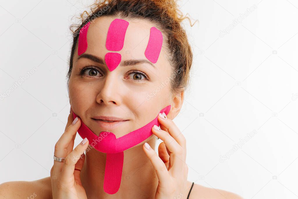 Young woman with pink anti-wrinkle cosmetic tape on her face over white. Double chin reducing.
