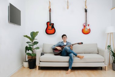Bardaklı neşeli bir adam gitarla poz veriyor, oturma odasında bir kanepede oturuyor. Düşük ihtimal.