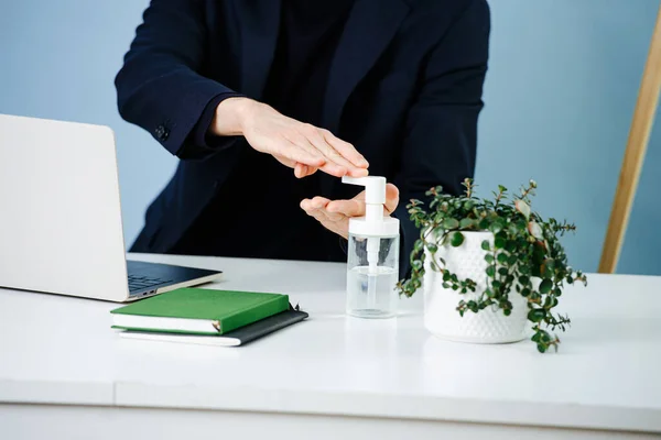 Man working in an office during covid-19 pandemic. He is disinfecting his hands before touching anything on his work desk. Close up, cropped, no head.