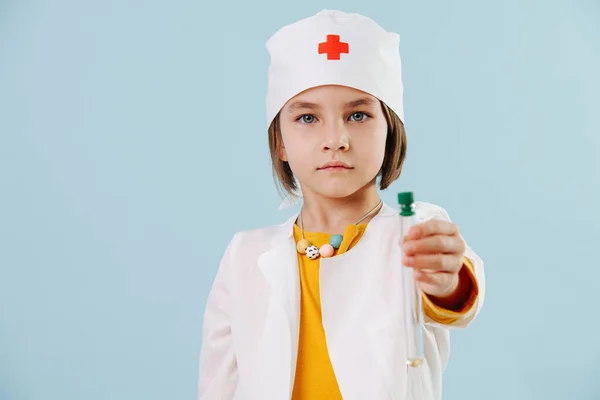 Little girl playing a doctor over blue background. Pandemic inspired. Child dreams to be a doctor to save peoples lives from coronavirus. Holding test-tube with colored liquid.