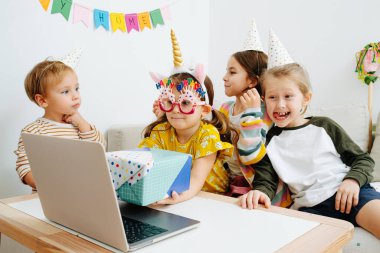 Dört küçük çocuk evde karantinada online doğum günü partisi veriyor. Dizüstü bilgisayarın önünde parti şapkası takarak kutluyorlar. Web kamerasında hediyeler gösteriliyor.