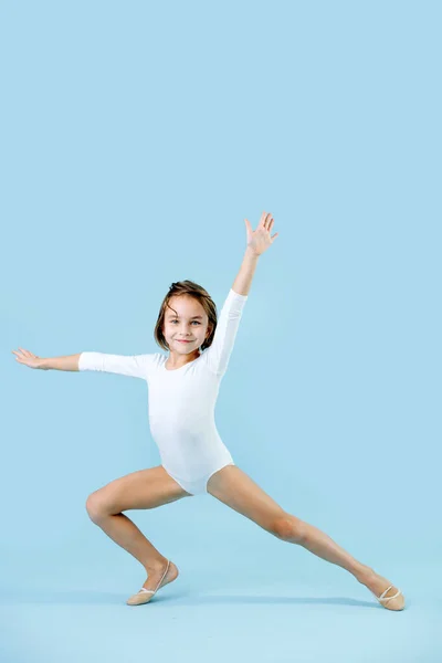 穿着白色紧身衣的小黑发女孩在蓝色背景上做体操 满面春风 一定要取悦和打动人 — 图库照片