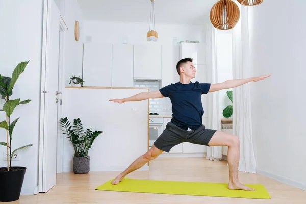 Tall man doing yoga on a mat in a kitchen at home during isolation. warrior form variation