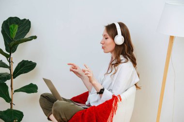 Evde kulaklıklı bir kız elinde dizüstü bilgisayarla oturmuş video bağlantısıyla iletişim kuruyor.