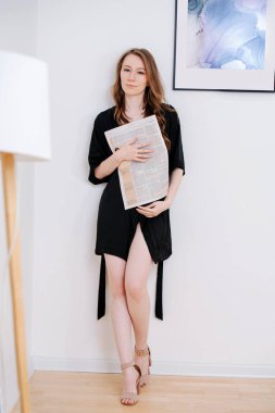 Duvara dayanmış kısa siyah bornozlu tahrik edici genç bir kadının portresi..