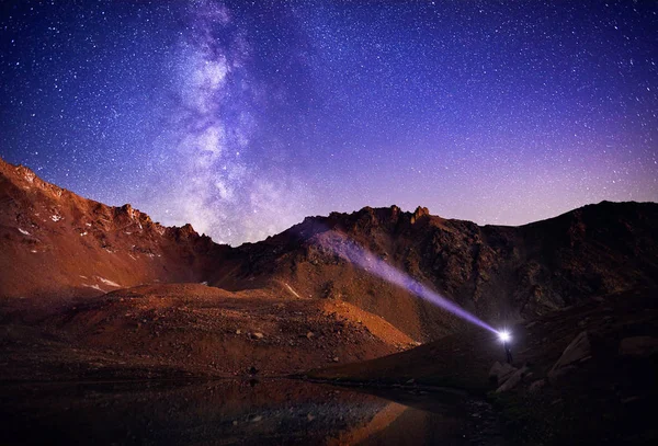 Man met koplamp in de bergen bij nachtelijke hemel — Stockfoto