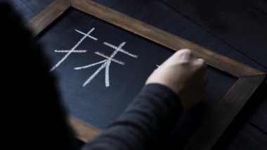 Kadın tahtaya Japon sembolleri yazıyor.